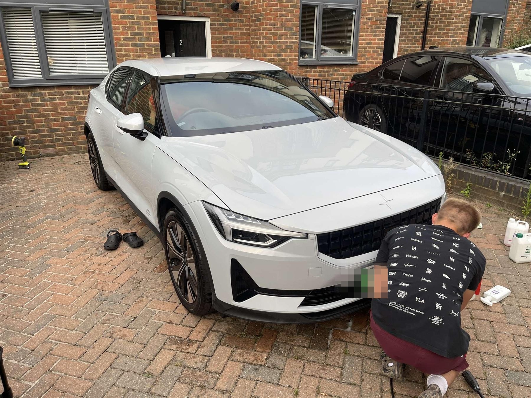 Detailer working by hand on the front of a white Polestar 2